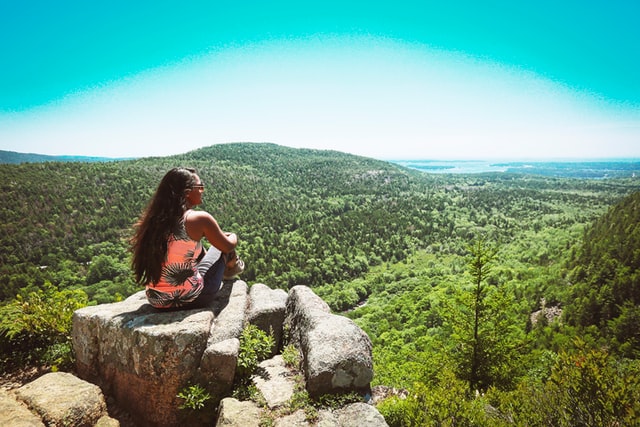 woman sitting on a rock atop a mountain overlooking vegetation